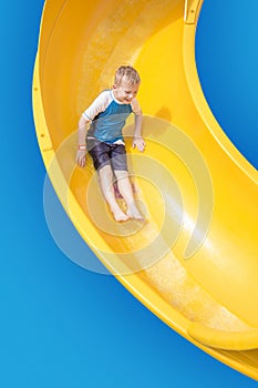 Smiling Young boy riding down a yellow water slide