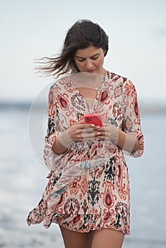Smiling young brunette caucasian woman chatting on a red mobile phone in the beach. People lifestyle concept