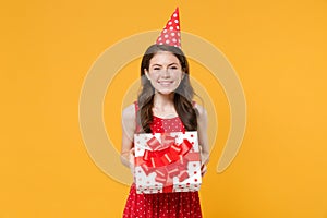 Smiling young brunette woman girl in red summer dress, birthday hat posing isolated on yellow background. Birthday