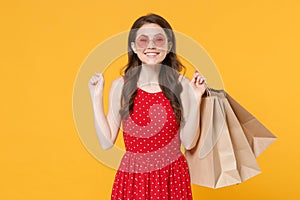 Smiling young brunette woman girl in red summer dress, eyeglasses posing isolated on yellow wall background. People