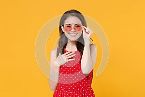 Smiling young brunette woman girl in red summer dress, eyeglasses posing isolated on yellow wall background studio