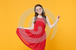 Smiling young brunette woman girl in red summer dress, eyeglasses posing isolated on yellow wall background studio