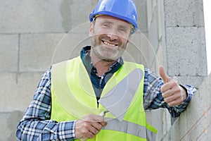 Smiling young builder in hardhat showing thumbs up