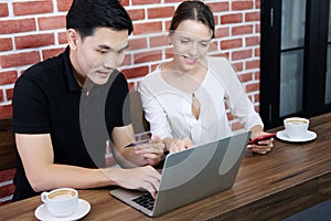 Smiling young business couple loves Asian man and caucasian woman holding credit card for online shopping and paying in social