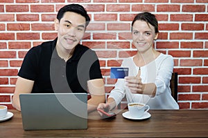 Smiling young business couple loves Asian man and caucasian woman holding credit card for online shopping and paying in social