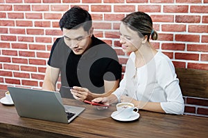 Smiling young business couple loves Asian man and caucasian woman holding credit card for online shopping and paying in social