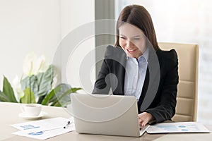 Smiling young business lady working with laptop, looking at scre