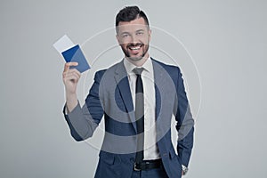 Smiling young business man in classic black suit, shirt hold passport, boarding pass ticket isolated on grey wall background in