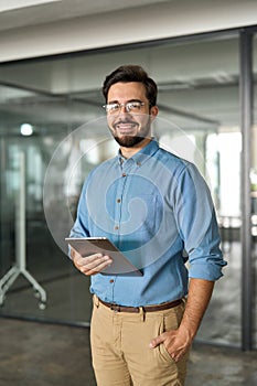 Smiling young business man manager with tab standing in office. Portrait.