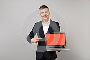 Smiling young business man in suit pointing index finger on laptop pc computer with blank empty screen isolated on grey