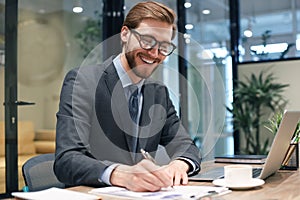 Smiling young business man writing something down while working in modern office