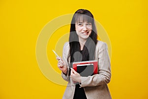 Smiling young business woman in a gray jacket holding pen over yellow