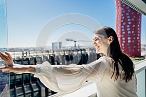 Smiling young business woman opening up a window for the view.Hotel room in business/industrial area.Conference complex.Business