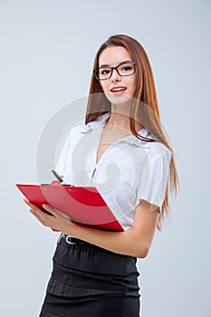 The smiling young business woman with pen and tablet for notes on gray background