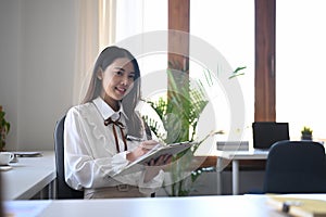 Smiling business woman sitting at her workplace and reading document.