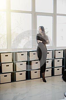 Smiling young business woman standing with folded arms in office. Woman in formal business attire standing in front of her desk in