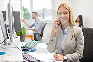 Smiling young business woman talking on mobile phone while sitting in office.