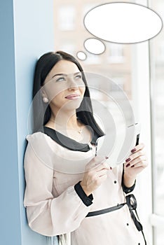 Smiling young business woman using tablet PC while standing relaxed near window at her office