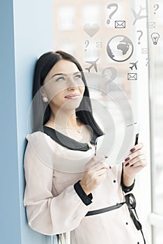 Smiling young business woman using tablet PC while standing relaxed near window at her office