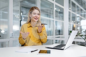 Smiling young business woman working in the office on a laptop, sitting at the table and talking on the phone through