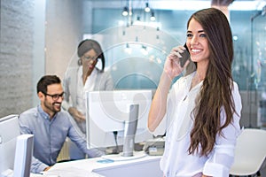 Smiling young business woman talking on mobile phone in office