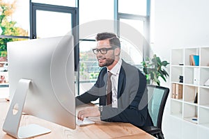 smiling young businessman in eyeglasses using desktop computer