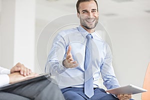 Smiling young businessman gesturing while sitting at office during meeting
