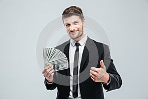 Smiling young businessman holding money and showing thumbs up