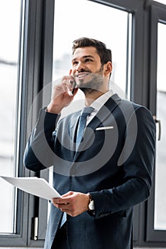 smiling young businessman holding papers and talking on smartphone