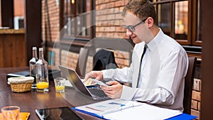 Smiling young businessman making a call with his smartphone in a restaurant.