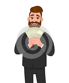 Smiling young businessman showing or holding cash, money, currency notes, dollars or banknotes in hands. Business, finance.
