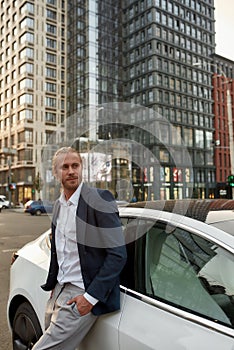 Smiling young businessman standing near white car