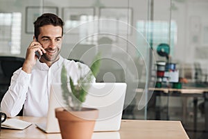 Smiling young businessman talking on a cellphone in an office