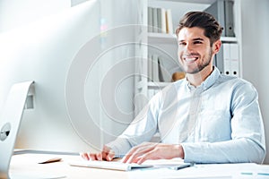 Smiling young businessman using laptop computer in office