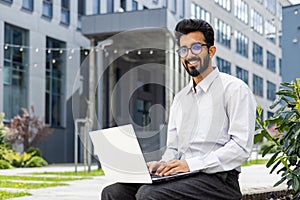 Smiling young businessman working on laptop outdoors in the city