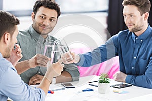 Smiling young businessmen drinking water and discussing new project