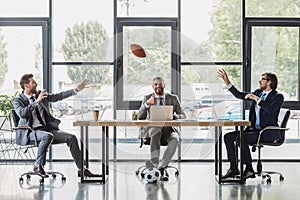smiling young businessmen using laptops and playing with soccer and rugby balls