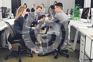 Smiling young businesspeople clinking cups while sitting together during coffee break