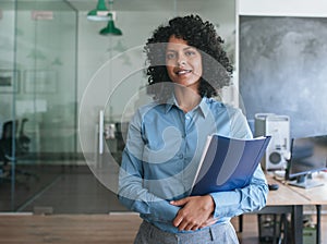 Smiling young businesswoman carrying paperwork while standing in an office