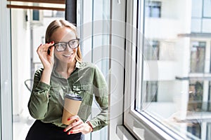 Smiling young businesswoman holding a coffee cup and looking out the window