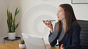 Smiling young businesswoman using voice recognition function on a smartphone