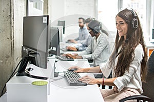 Smiling young businesswoman working with colleagues in a call center office, technical support operators.