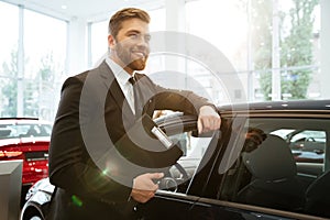 Smiling young car salesman standing at the dealership