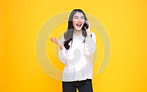 Smiling young casual Asian woman talking smart phone isolated over yellow background