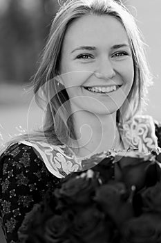 Smiling young caucasian bride, lightweight dress posing. Wedding bouquet in her hands. Black and white photo.