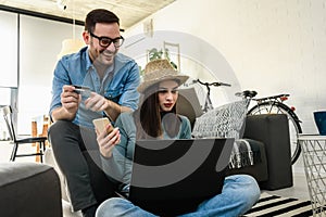 Smiling young Caucasian couple shopping online at home using a laptop with a credit card