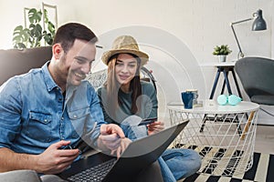Smiling young Caucasian couple shopping online at home using a laptop with a credit card