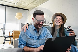 Smiling young Caucasian couple shopping online at home using a laptop with a credit card