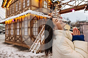 Smiling young caucasian girl laughing with closed eyes walks at amusement park during New Year.