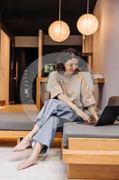 Smiling young caucasian girl uses modern laptop sitting on sofa.